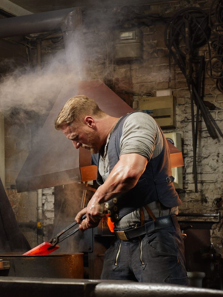 a man working in a metal shop with steam coming out of his mouth and holding a large spatula