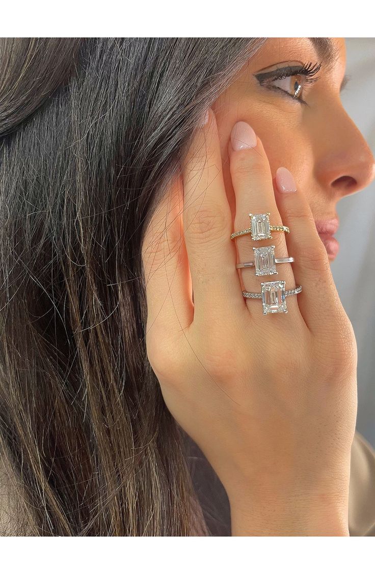 a woman holding her hand up to her ear with three diamond rings on top of it