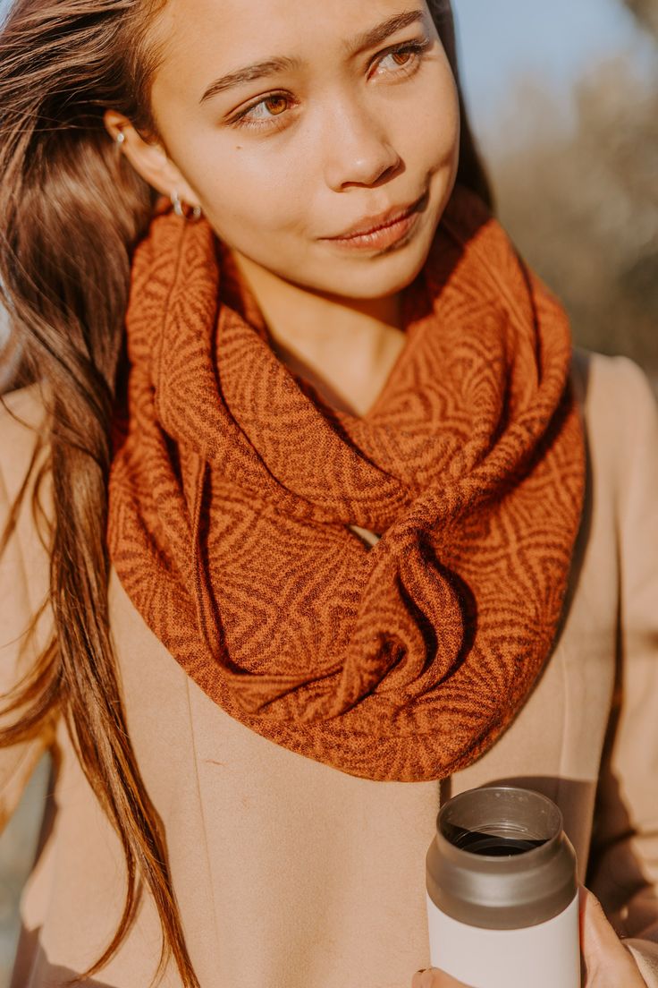 a woman wearing an orange scarf and holding a white coffee cup in her right hand