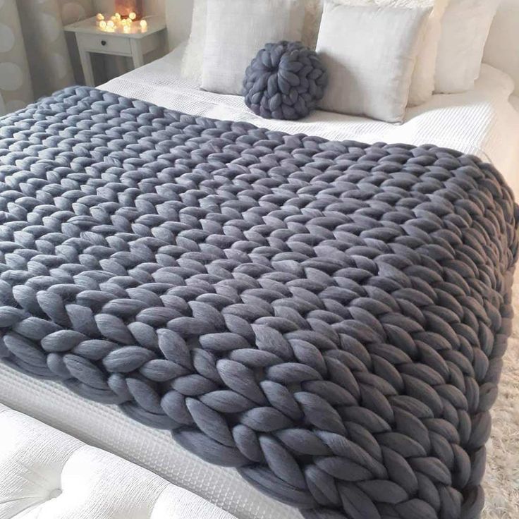 a large gray blanket sitting on top of a bed next to two white pillows in a bedroom