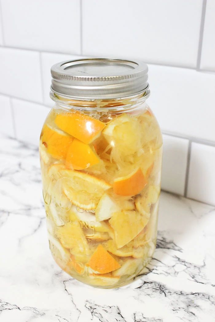 a glass jar filled with sliced oranges on top of a marble counter next to a white tile wall