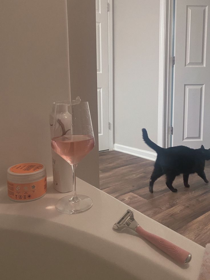 a black cat standing next to a bath tub filled with pink liquid and a toothbrush