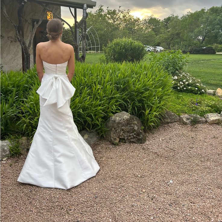 a woman in a white wedding dress is looking at the grass and bushes behind her