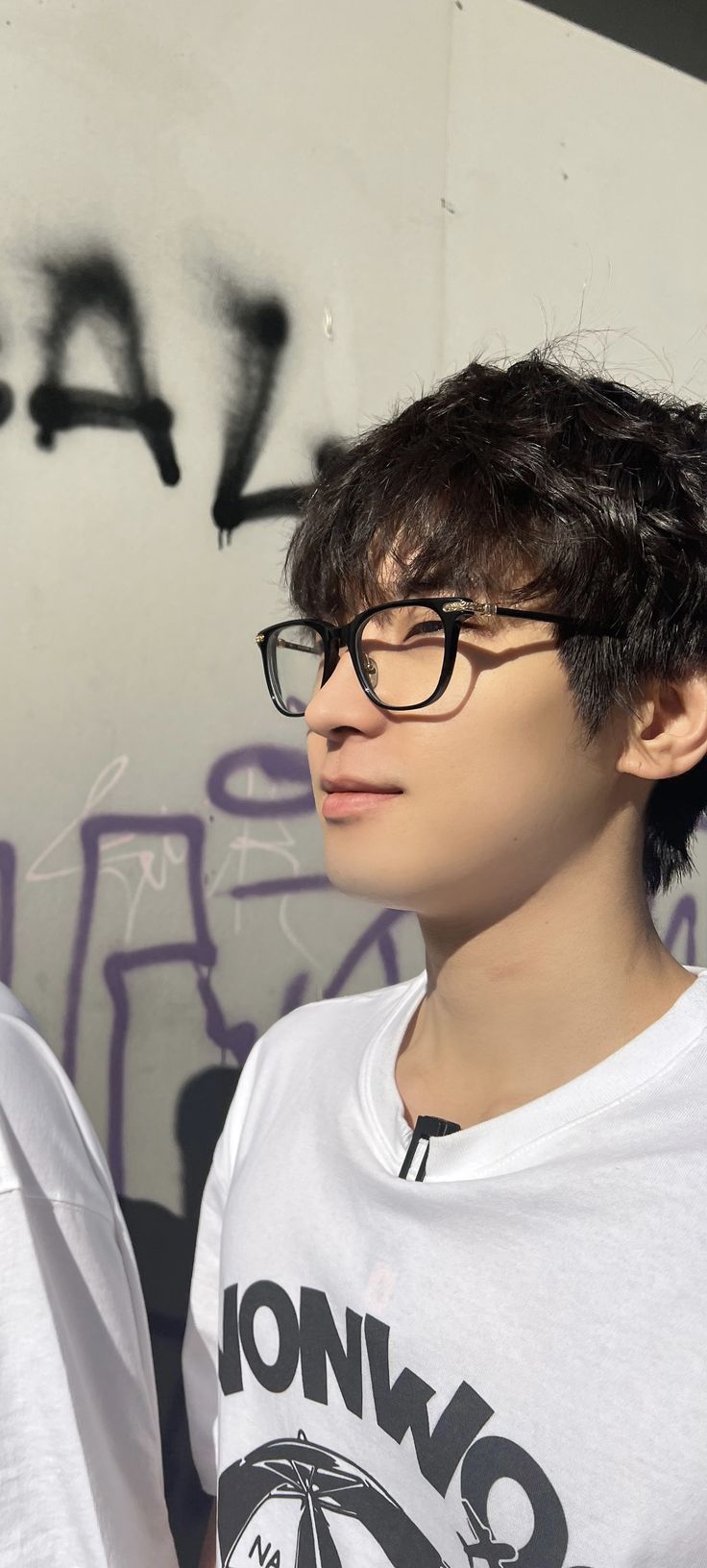 a young man wearing glasses standing in front of a wall with graffitti on it