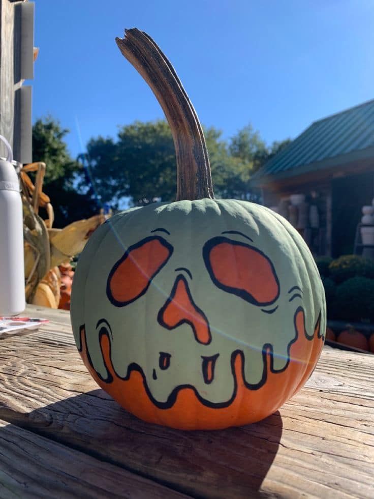 a pumpkin with a face painted on it is sitting on a wooden table in front of a house