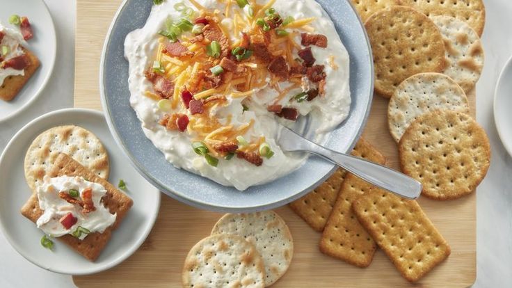 crackers, cheese and bacon spread on a plate with crackers next to them