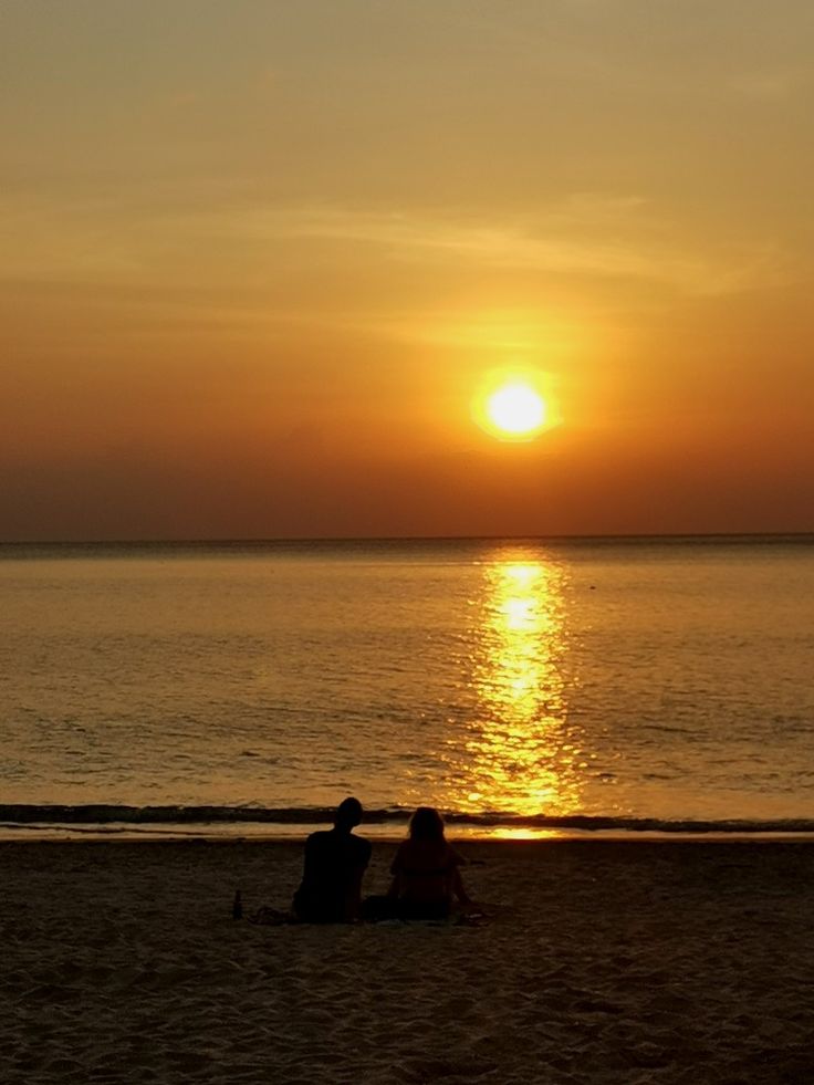 two people sitting on the beach at sunset