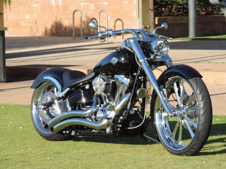 a black and chrome motorcycle parked on top of a lush green field next to a building