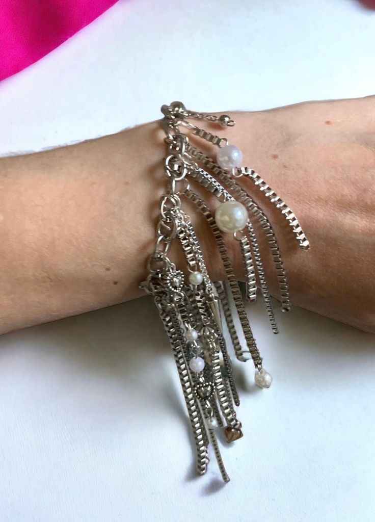 Fringed Chain Bracelet ⛓️ This stunning bracelet features a unique design that combines silver chains in different mediums with faux pearls. The result is a piece of jewelry that is both eye-catching and elegant. ⛓️ The bracelet is made with a variety of silver chains, including delicate curb chains and bolder link chains. The chains are fringed, creating a sense of movement and dimension. The faux pearls are interspersed throughout the chains, adding a touch of luxury and glamour. ⛓️ Only one a Elegant Silver Chain Bracelet With Beaded Chain, Elegant Silver Chain Bracelet With Beaded Details, Adjustable Metal Beaded Chain Charm Bracelet, Elegant Metal Chain Bracelet With Beaded Chain, Adjustable Metal Beaded Chain Bracelet, Elegant Metal Beaded Chain Bracelet, Trendy Silver Bracelet With Beaded Chain, Silver Pearl Bracelet With Jubilee Style For Party, Metal Charm Bracelet With Adjustable Chain For Party