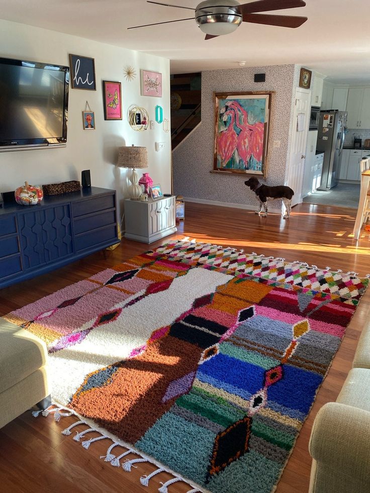 a living room filled with furniture and a flat screen tv mounted on the wall above a colorful rug