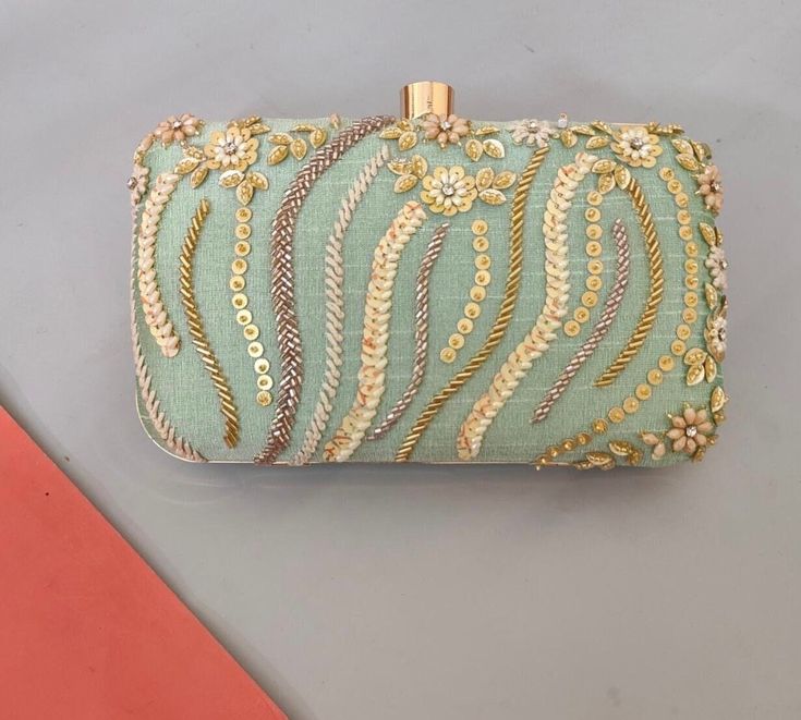 This is a beautiful handcrafted clutch bag made with love.It has intricate handwork which showcases the Indian craftsmanship by our local artisans. It comes with a metal sling chain. Details  - Single side handwork  - Fabric lining on the inside to keep your belongings safe  - Metal lock closure  - Detachable sling chain  This clutch can be worn as a crossbody bag or a shoulder bag with the sling chain or can simply be carried in hand.It is spacious enough to carry mobile phones, lipsticks, Keys Asian Gifts, Indian Gifts, Embroidered Clutch, Wedding Accessory, Bride Gift, South Asian, Evening Clutch, Local Artisans, Small Accessories