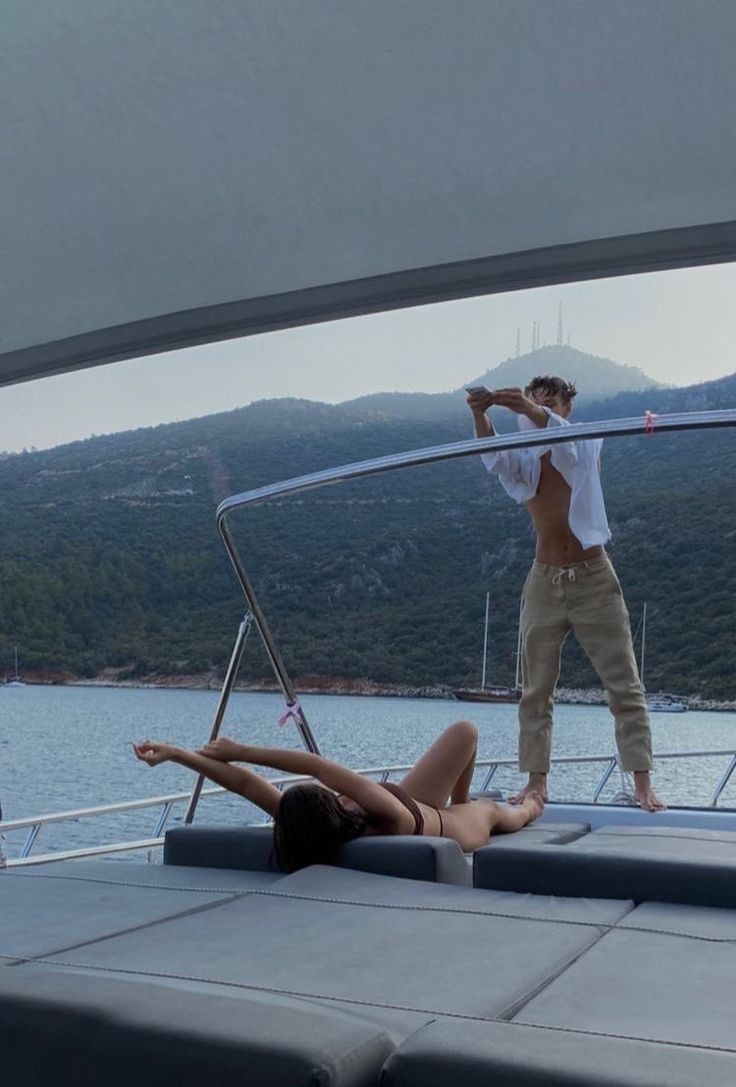 a man standing on the back of a boat next to a woman laying on it