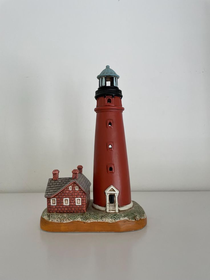 a red and white lighthouse with a small house on it's base, sitting on a table