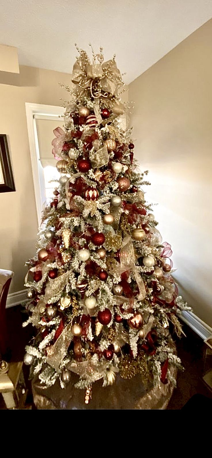 a white christmas tree with red and gold ornaments on it in a living room area