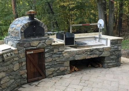 an outdoor grill made out of stone and wood with a pizza oven on the side