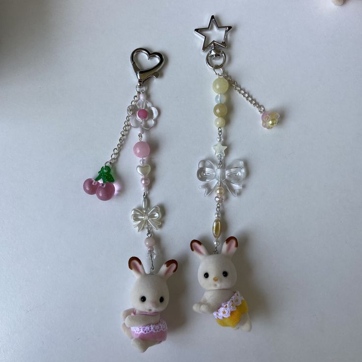 two key chains with charms attached to them on a white surface, one has a bunny and the other is a rabbit holding an egg