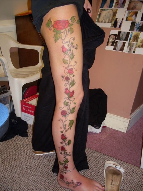 a woman's leg with flowers and vines on it, next to her shoes