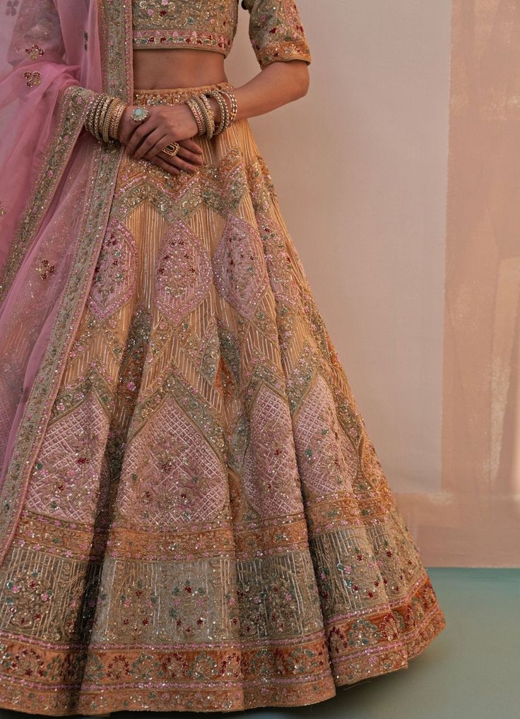 Features a gold organza double dupatta lehenga set embroidered with traditional zardozi technique using silken threads, dabka, cutdana and sequins highlighted with multiple pastel hued velvet appliques. Completed with two dupattas in rust gold and pink for your big day. Composition : Lehenga, Blouse and Dupatta- Organza, Velvet Care: Dry Clean Only and Vacuum Storage This product can be customised for sleeves, length of blouse and neckline Delivery : 6-8 weeks as the product is hand crafted. Check Size Guide or choose MySize for free customisation (All Sizes above XL can be made at 15% additional cost) For more information and sizes please contact fabiliciousfashion@gmail.com or visit our Copenhagen studio.About the Designer : Angad Singh's journey in the world of fashion started with at a Gold Semi-stitched Gown With Dori Work, Traditional Eid Gown With Dori Work, Traditional Gold Art Silk Gown, Semi-stitched Kundan Gown With Zari Work, Traditional Cutdana Gown For Reception, Traditional Gold Gown With Pallu, Traditional Gold Gown With Cutdana, Traditional Gold Gown With Cutdana Detail, Semi-stitched Raw Silk Gown With Dori Work