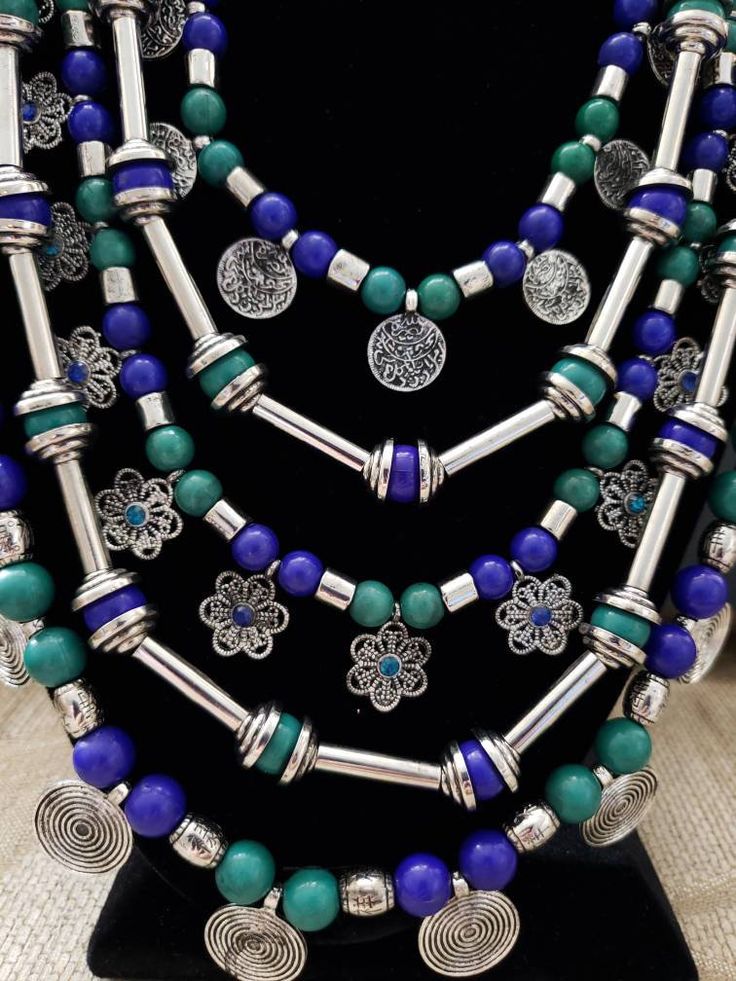 Gather compliments wearing this handcrafted multi strand colorful Afghani Kuchi coin necklace in a silver color. This is a LOT of necklace! Five strands. Outer row has stamped circular discs in an eternity pattern, middle row has adorable filigree flowers with colored centers, and the inner row has stamped discs resembling coins. Between each row is a row of beads separated by long tubular silver colored beads. Beads attach at the top to a beautiful peacock motif, and then a pretty chain. Lobste Handmade Silver Bohemian Coin Necklace, Handmade Bohemian Metal Layered Necklace, Handmade Metal Bohemian Layered Necklace, Silver Bohemian Coin Necklace For Festivals, Bohemian Silver Coin Necklace For Festivals, Bohemian Necklace With Nickel Free Round Beads, Unique Silver Multi-strand Beaded Necklaces, Silver Bohemian Adjustable Layered Necklace, Bohemian Multicolor Nickel-free Beaded Necklaces