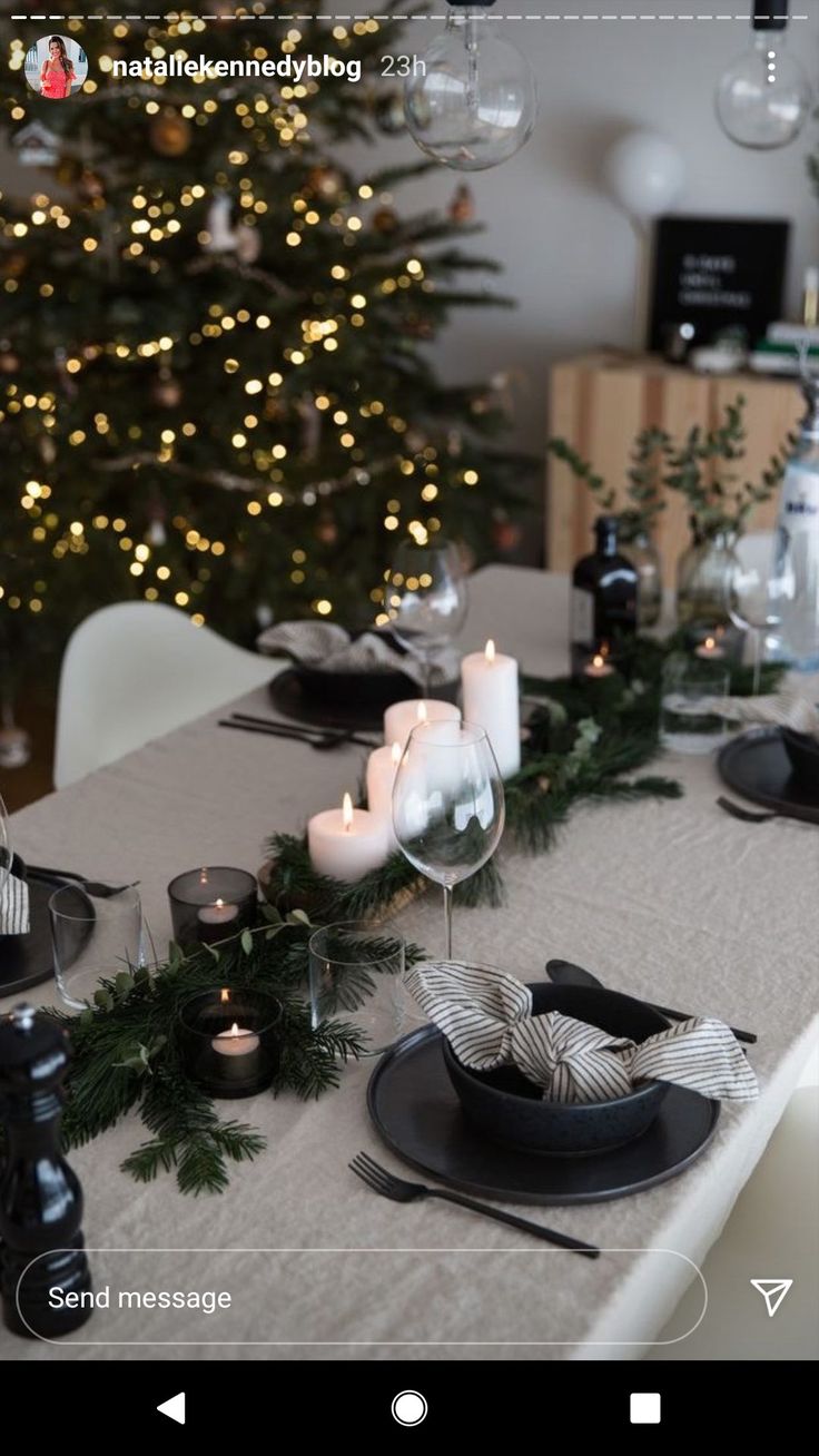 a christmas table setting with candles, plates and silverware in front of a tree