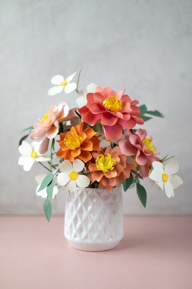 a white vase filled with lots of colorful flowers on top of a pink countertop