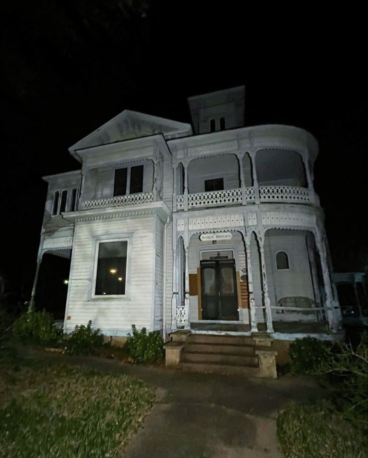 a large white house sitting on the side of a road at night with its lights on