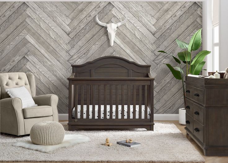 a baby's room with a crib, chair and cow skull on the wall