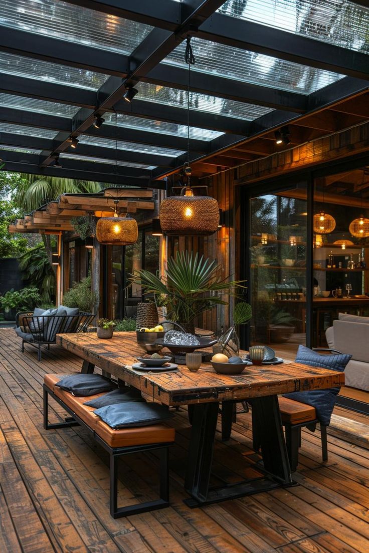 an outdoor dining area with wooden flooring and glass roof over the table is lit by hanging lights