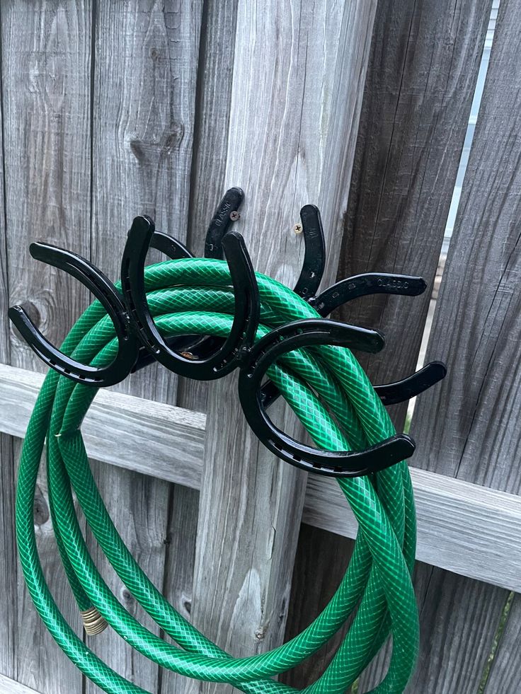 there is a green hose hanging from the side of a fence with two black handles