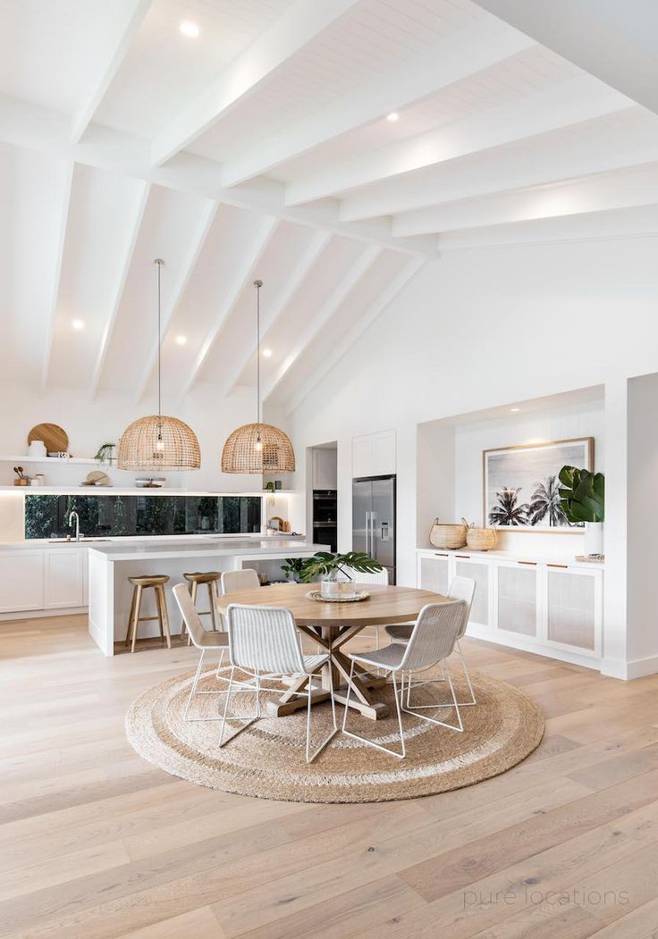 a large open kitchen and dining room area with white walls, wood flooring and vaulted ceiling