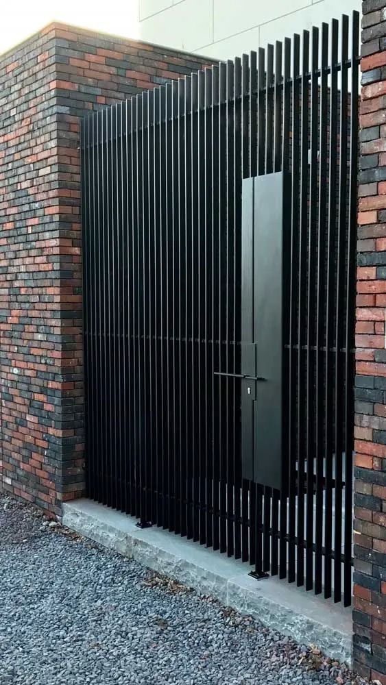 a black gate is in front of a brick wall with bars on the top and bottom