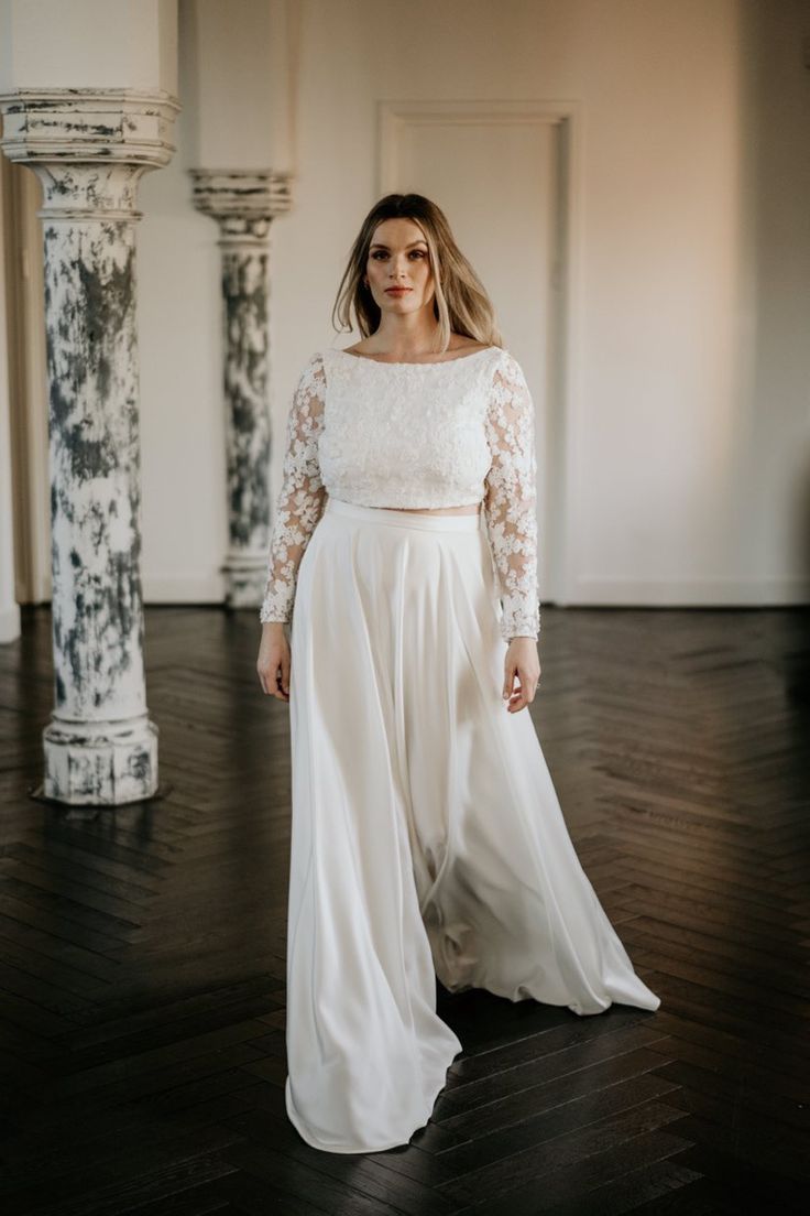 a woman standing in a room wearing a long white dress with sheer sleeves and an open back