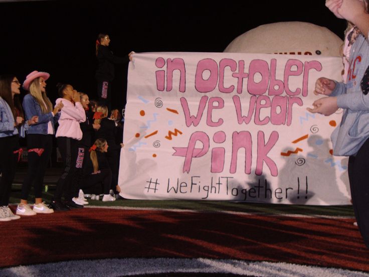 a group of young people standing next to a sign that says in october we wear pink