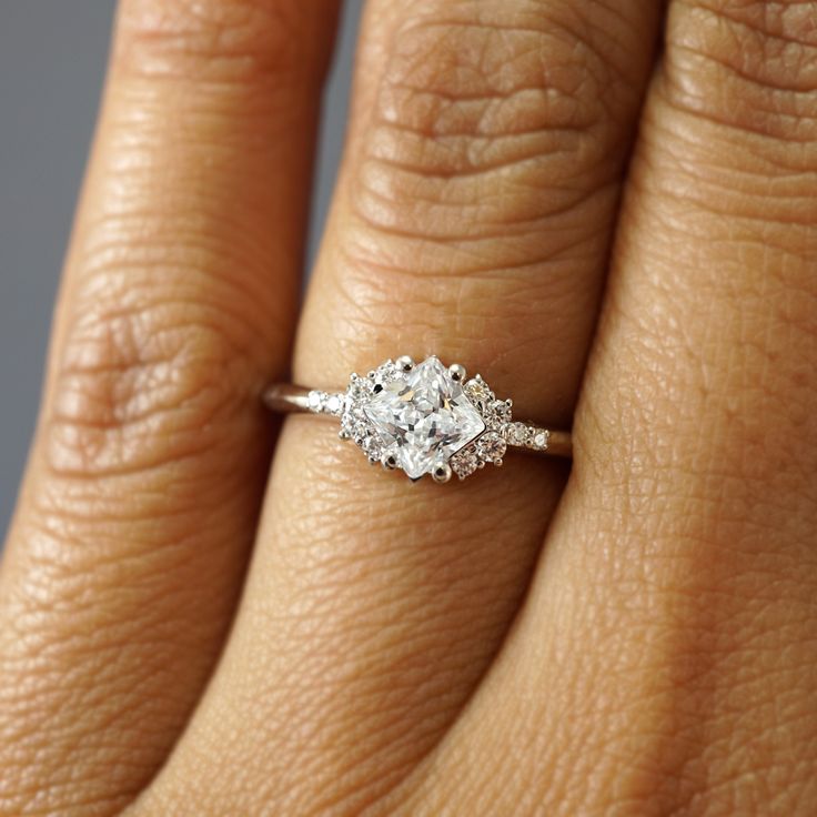 a woman's hand with a diamond ring on her left hand and the other hand holding an engagement ring