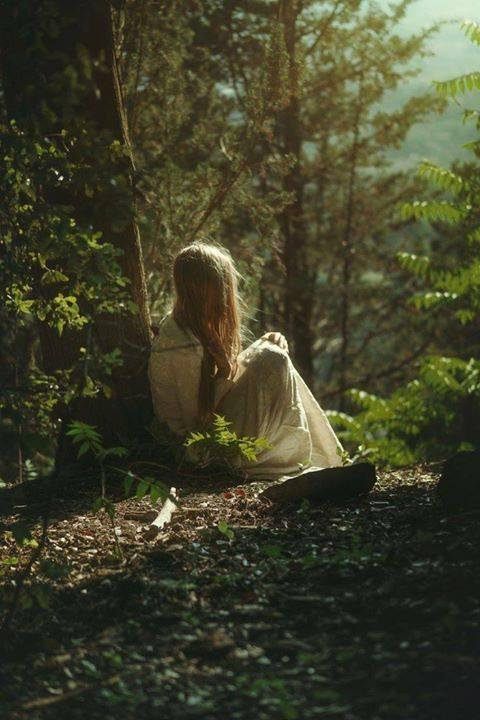 a woman sitting in the woods with her back to the camera and looking at something