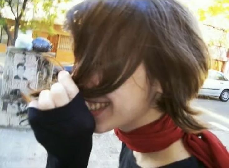 a woman is smiling and holding her hair up to her face as she walks down the street