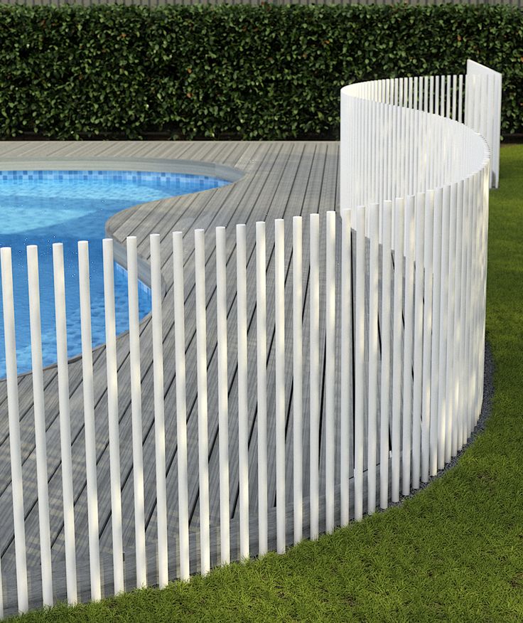 a white picket fence next to a swimming pool in a backyard with grass and shrubs