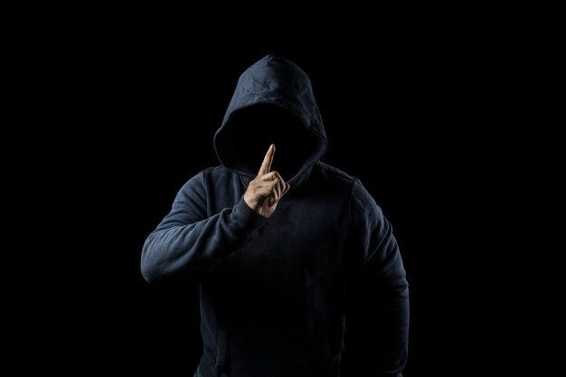 a man in a black hoodie making the peace sign with his hand while standing against a black background