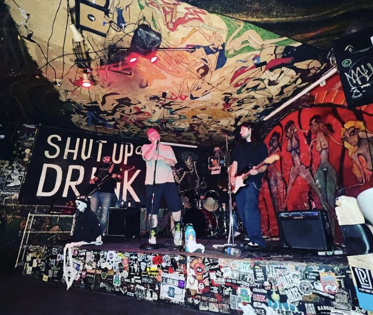 two men on stage with guitars and other musical instruments in front of graffiti covered walls