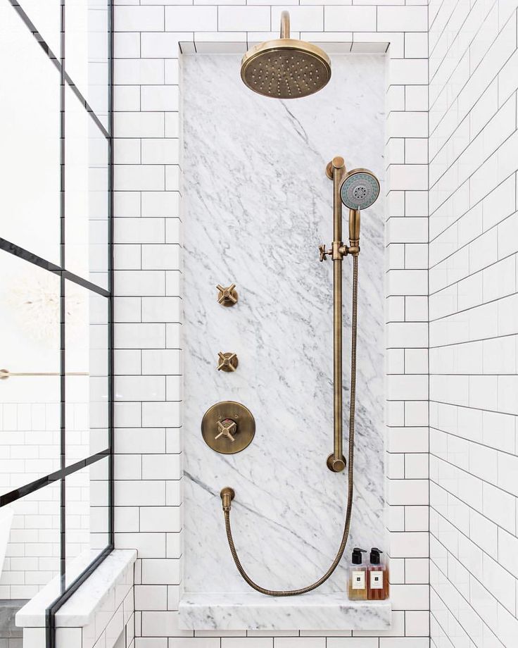 a bathroom with white subway walls and gold shower faucet in the shower area