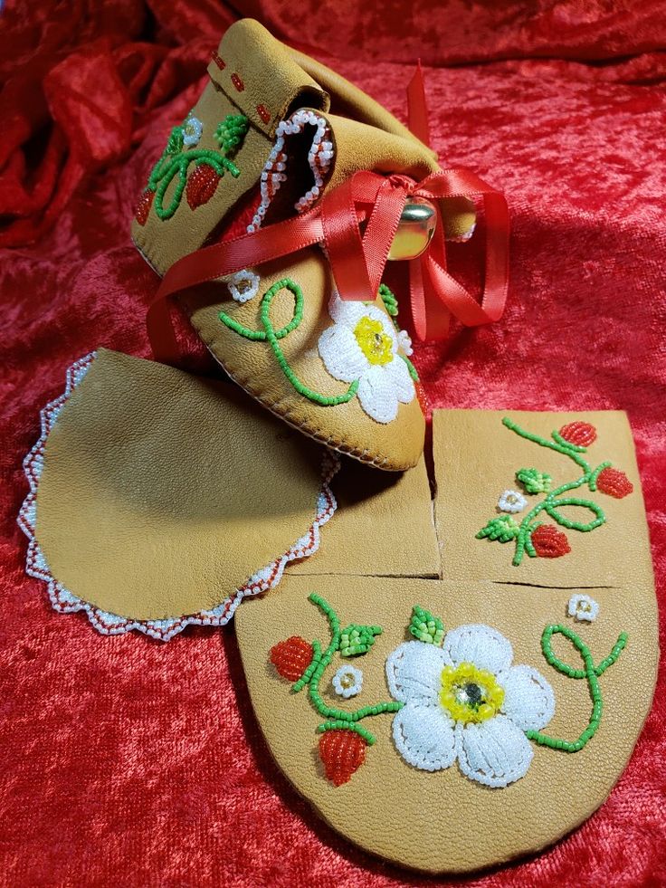 two pairs of baby shoes with flower appliqued on them, one is yellow and the other has red ribbon