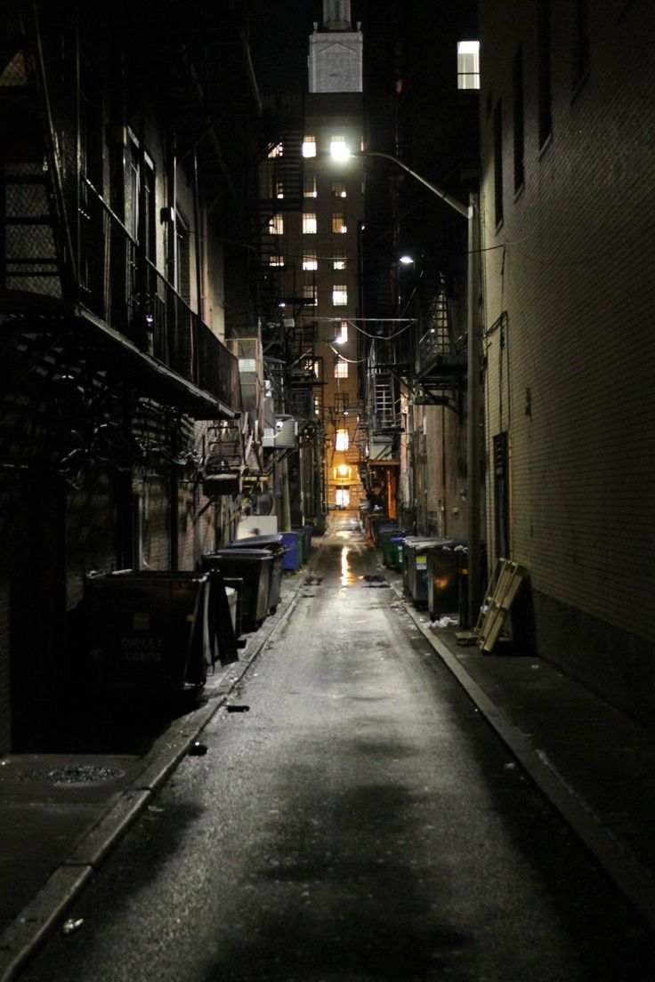 an alley way in the middle of a city at night with lights shining on it