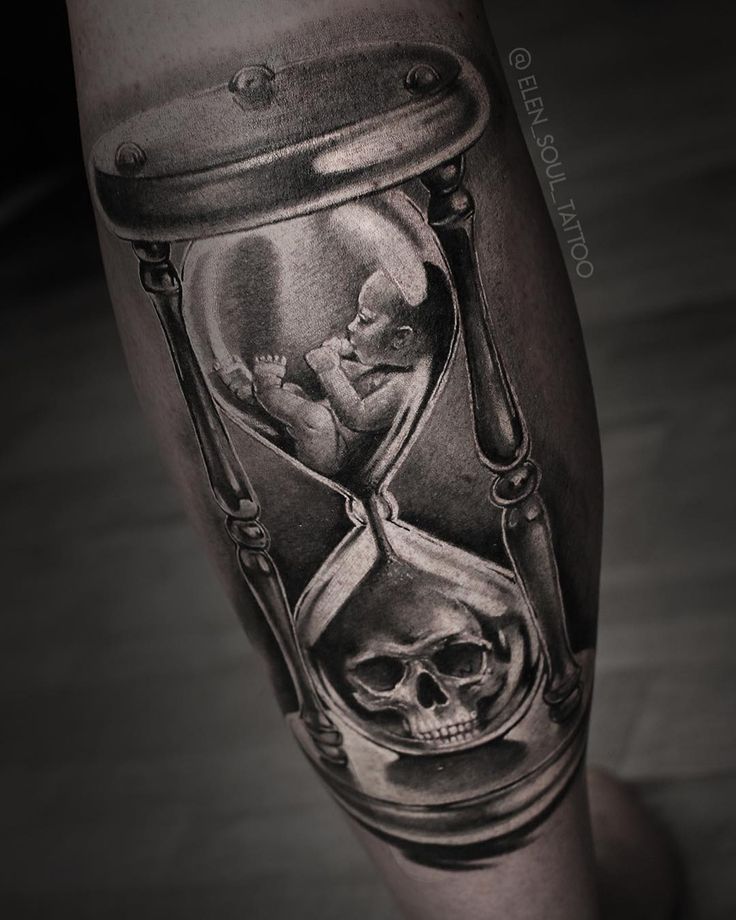 a man's leg with an hourglass tattoo on it and a skull in the sand