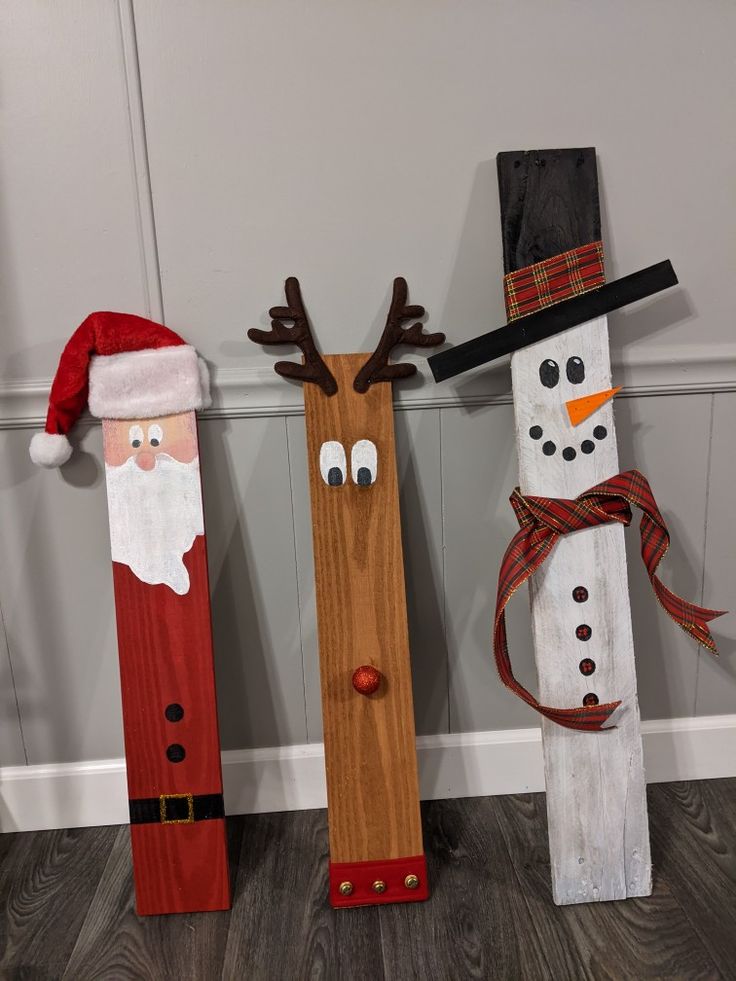 three wooden snowmen with santa hats and noses on them, standing next to each other