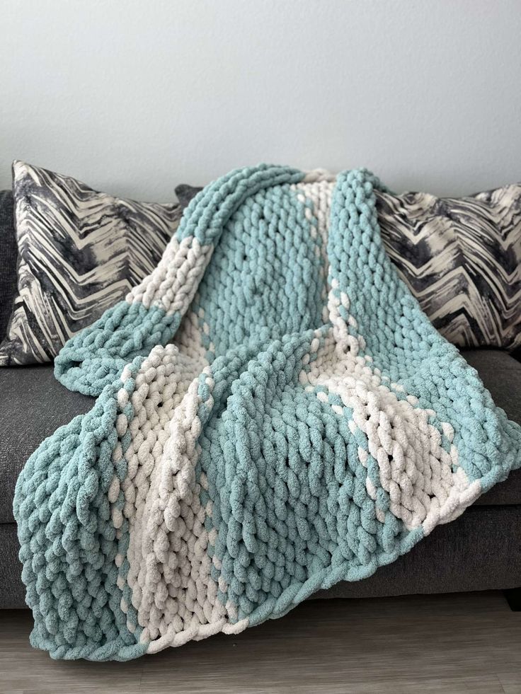 a blue and white knitted blanket sitting on top of a couch next to pillows