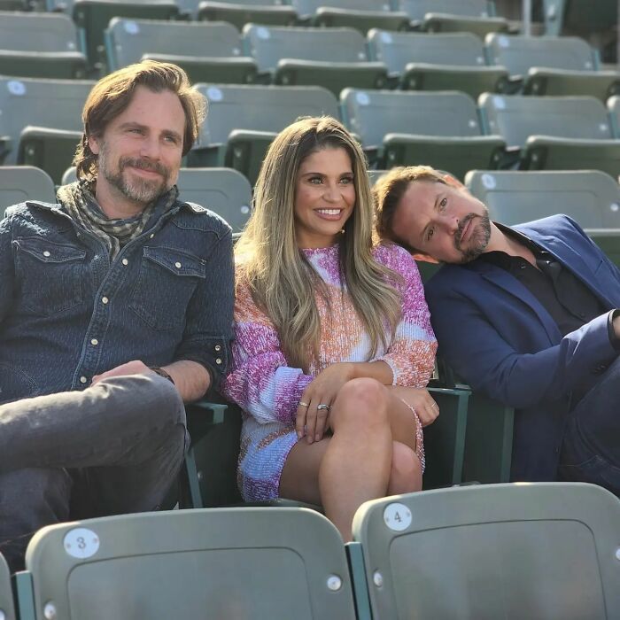 two men and a woman are sitting in the stands at a baseball game, smiling