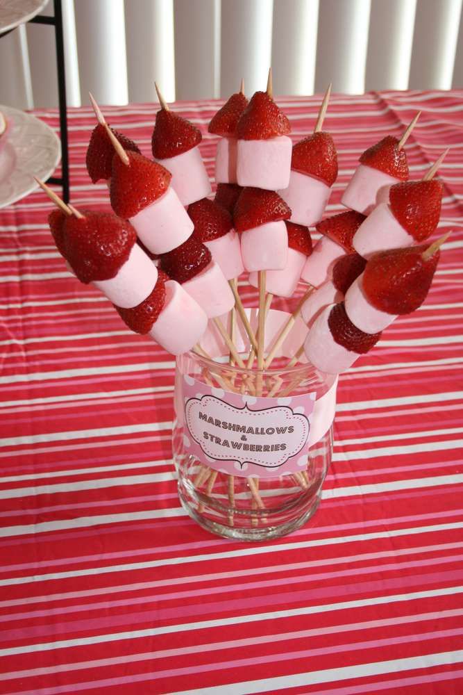 strawberries are arranged on skewers in a glass vase with candy sticks sticking out