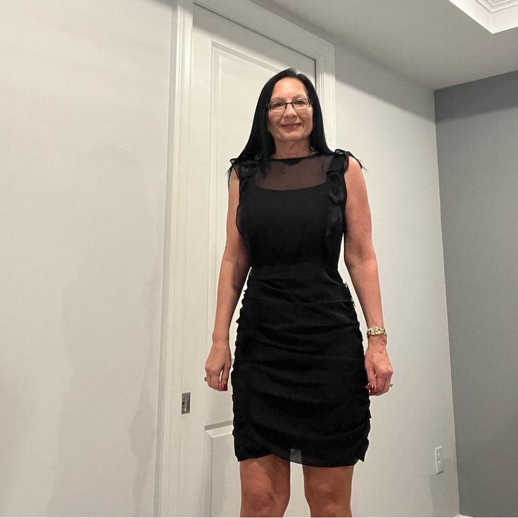 a woman standing in front of a white door wearing a black dress with sheer shoulders