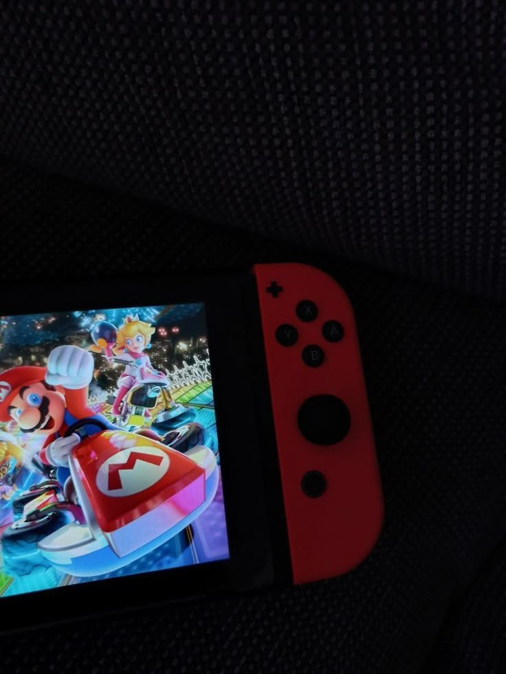 a red nintendo wii game controller sitting on top of a black couch next to an image of mario kart