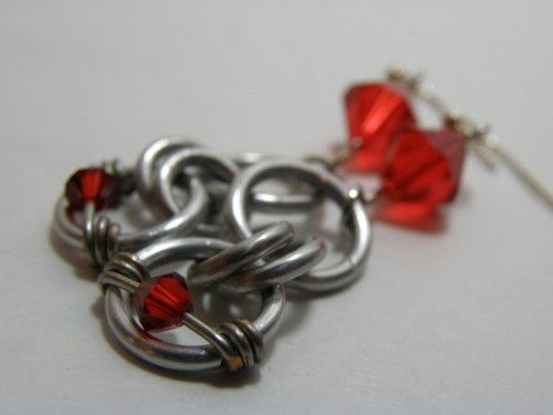 a pair of red glass beads are attached to silver chain link earrings on a white surface